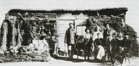 Une famille de colons devant sa cabane isolée avec des mottes de terre.